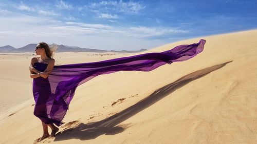 Woman with umbrella on sand at desert against sky