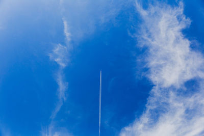 Jet with vapor trails soaring through light clouds in a blue sky.