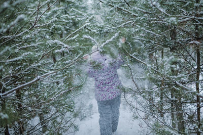 Woman standing amidst trees in forest during winter