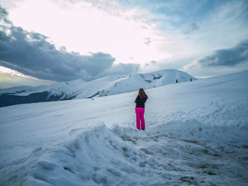 Rear view of woman standing on snowcapped mountain against sky