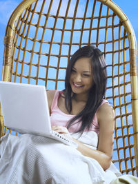 Smiling mid adult woman using laptop on wicker seat