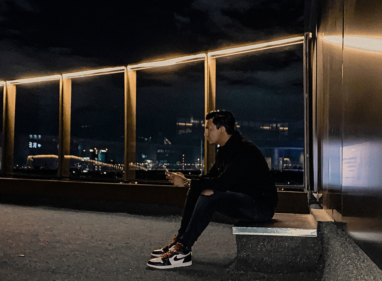 SIDE VIEW OF A YOUNG MAN SITTING ON SEAT