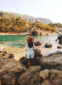 Rear view of woman standing on rocks at shore against sky