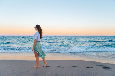 Rear view of woman standing at beach against clear sky