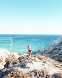 Woman standing on rock looking at sea against clear sky