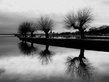 Silhouette trees by lake against sky