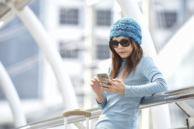 Young woman using phone while standing against railing