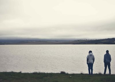 Rear view of people standing on shore against sky