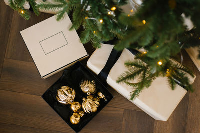 Christmas box is a stylish gift with a black bow on it and golden toys under the christmas tree