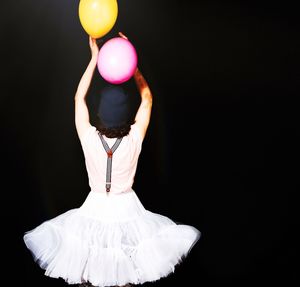Rear view of woman wearing tutu with balloons against black background