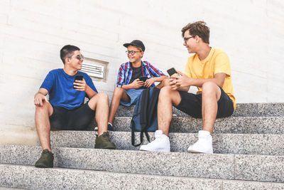 Smiling friends using smart phones while sitting on steps