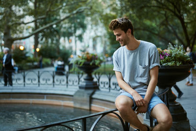 Young man sitting by fountain at park