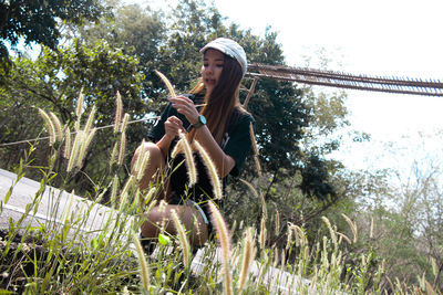 Side view of young woman sitting on plant against trees