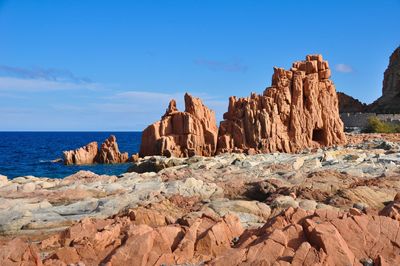 Rocks on shore by sea against blue sky