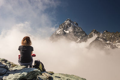 Rear view of woman sitting on rock against sky