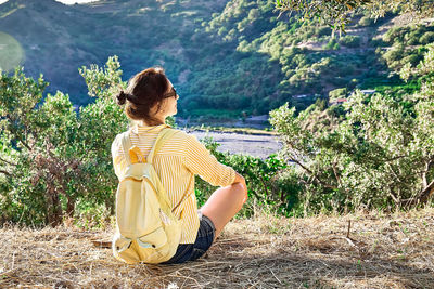 Woman resting in olive grove, enjoying mountain view, traveling with backpack
