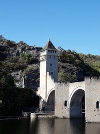 Arch bridge over river amidst buildings against clear blue sky