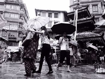 Low angle view of people holding umbrella while walking in city during rainy season 