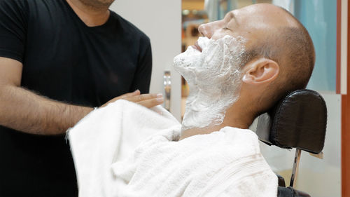 Barber applying shaving cream on mature man in salon