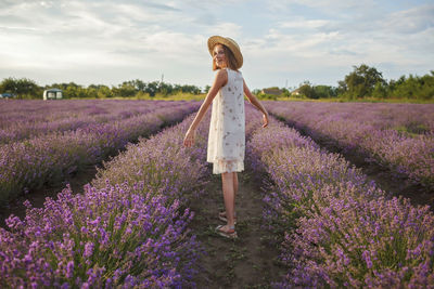 Rear view of woman standing on flowering plants on field against sky