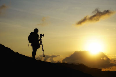 Silhouette person photographing on landscape against sky during sunset