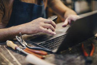 Midsection of upholstery worker using laptop while sitting at workbench in workshop