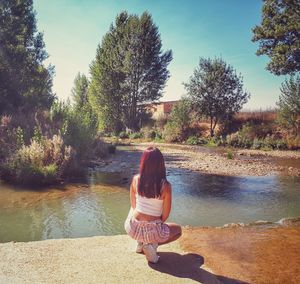 Rear view of woman sitting by lake against sky