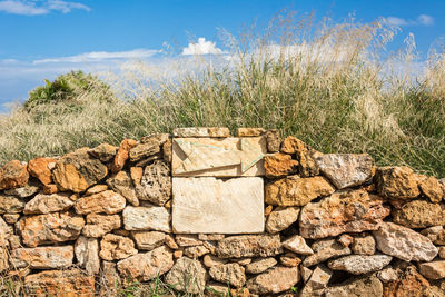 Stone wall by rocks on field against sky