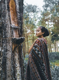 Side view of young woman looking at tree trunk