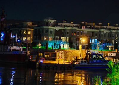Illuminated buildings by river against sky in city at night