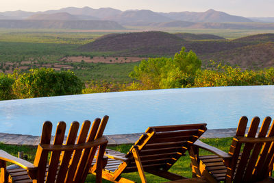 Empty chairs and tables by lake against mountains