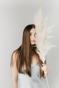 Attractive brunette woman hide face behind fluffy dry plant branch on light grey