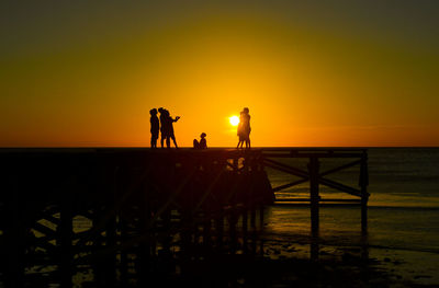 Silhouette people on beach against sky during sunset