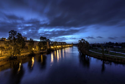 Illuminated bridge over river against cloudy sky