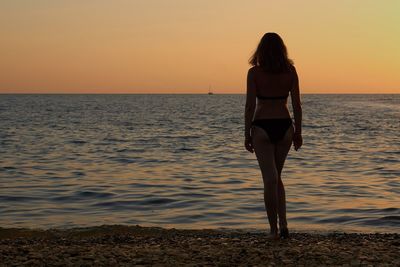 Rear view of woman standing on beach at sunset