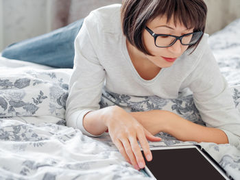 Woman in glasses are lying in bed with tablet. she is touching screen. morning bedtime.