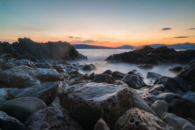 Scenic view of rocky shore against sky during sunset