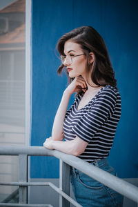 Side view of young woman looking away while standing by railing against wall