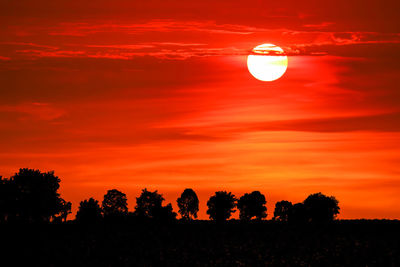 Silhouette trees on field against romantic sky at sunset