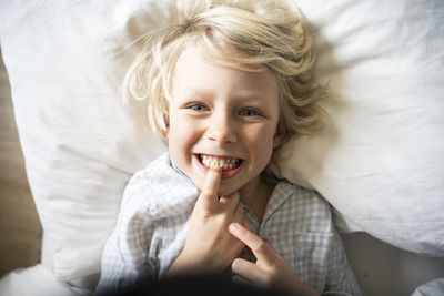 Happy boy touching and showing teeth on bed at home