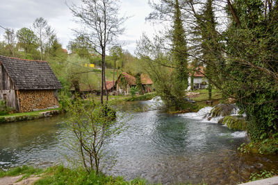 Scenic view of river by trees and houses against sky