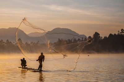 Men fishing on shore against sky during sunset