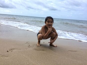 Full length portrait of playful boy crouching on shore at beach