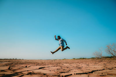Man jumping in desert against clear blue sky