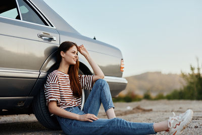 Young woman using mobile phone while sitting on car