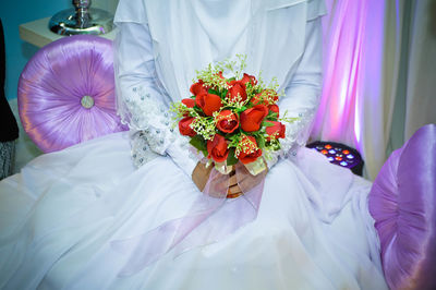 Midsection of bride holding artificial rose bouquet during wedding ceremony