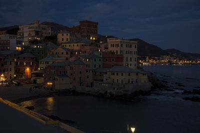 Illuminated buildings by sea against sky at night