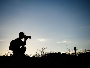 Silhouette man photographing against sky during sunset