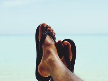 Low section of person wearing slipper at beach