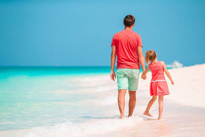 Rear view of siblings at beach against sky